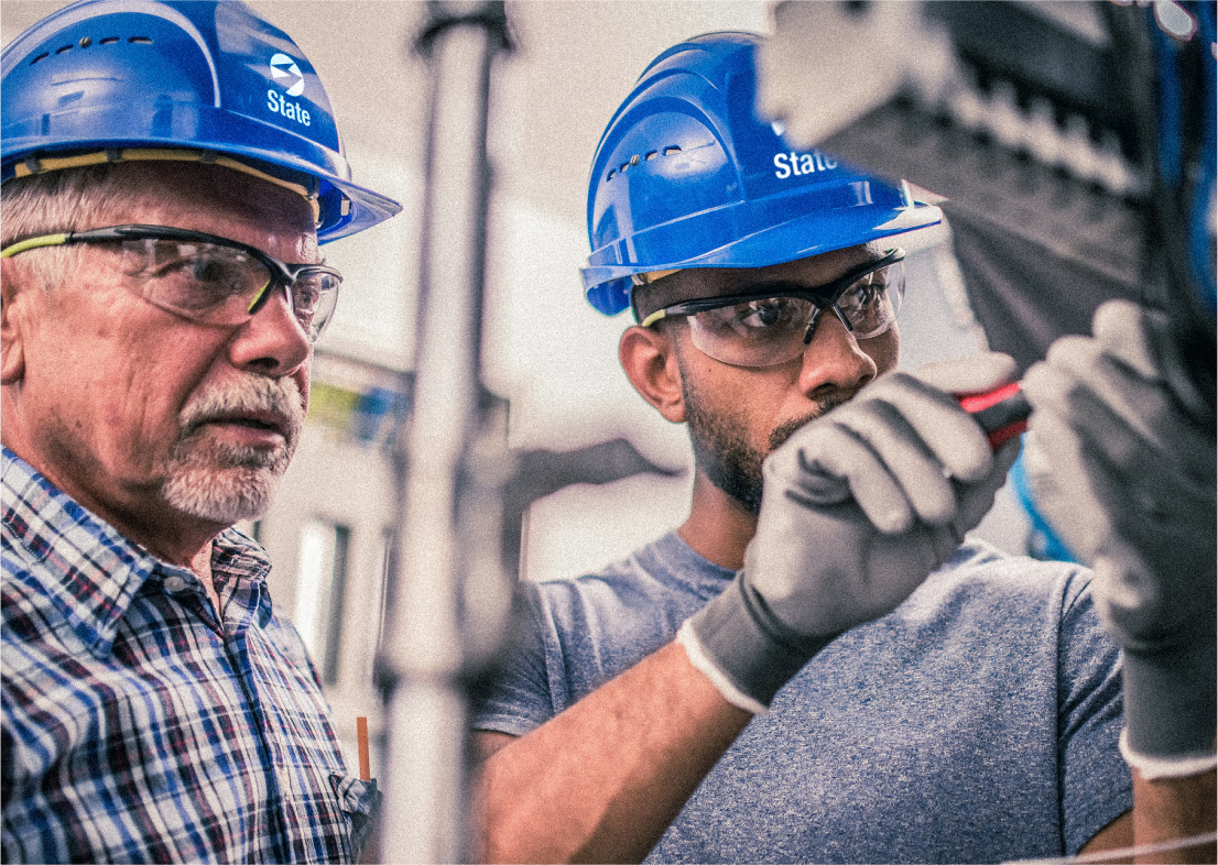 Two men wearing The State Group hats working